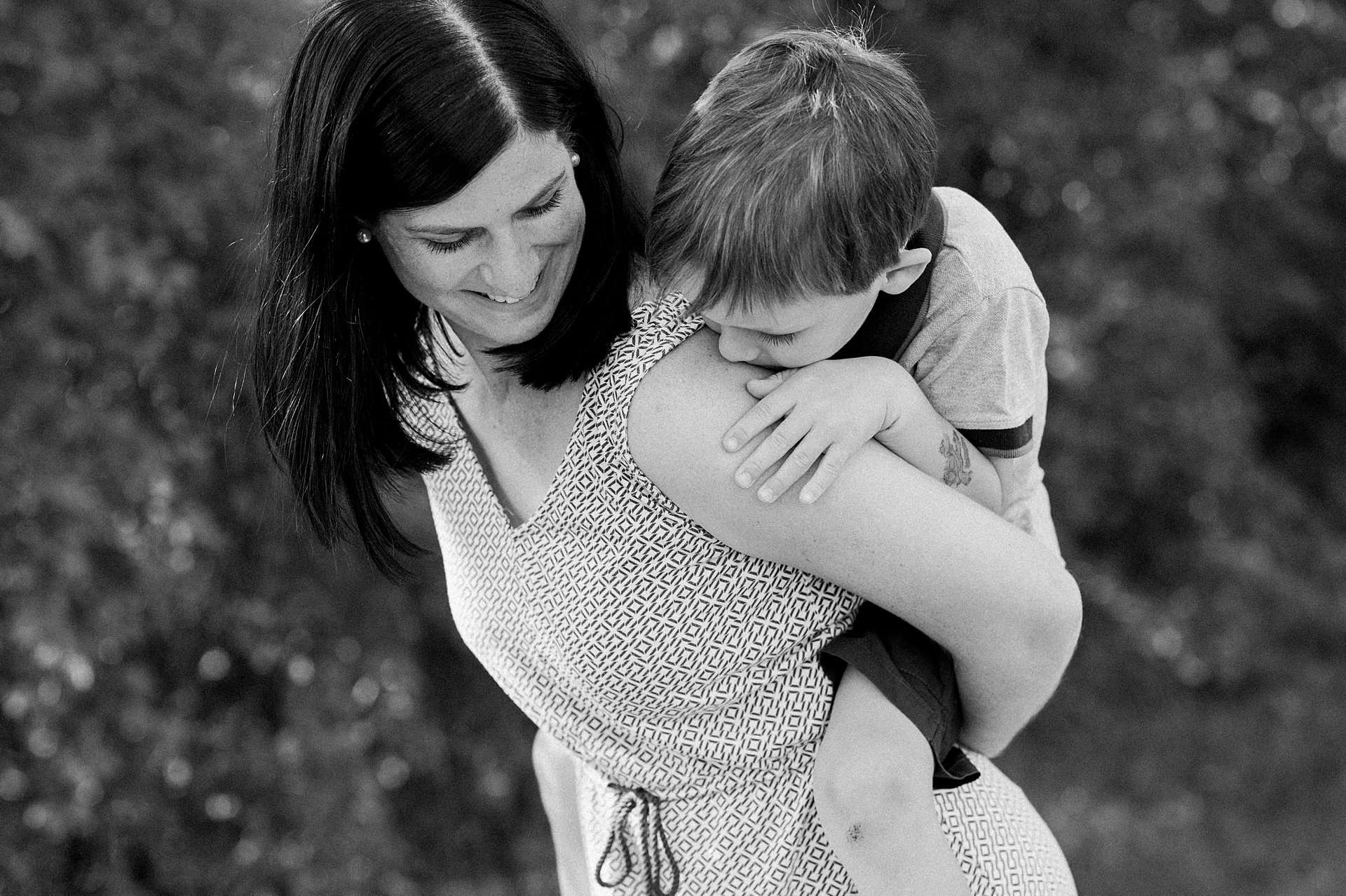 Schwarz-weiss Foto einer Mutter die ihren Sohn Huckepack trägt
